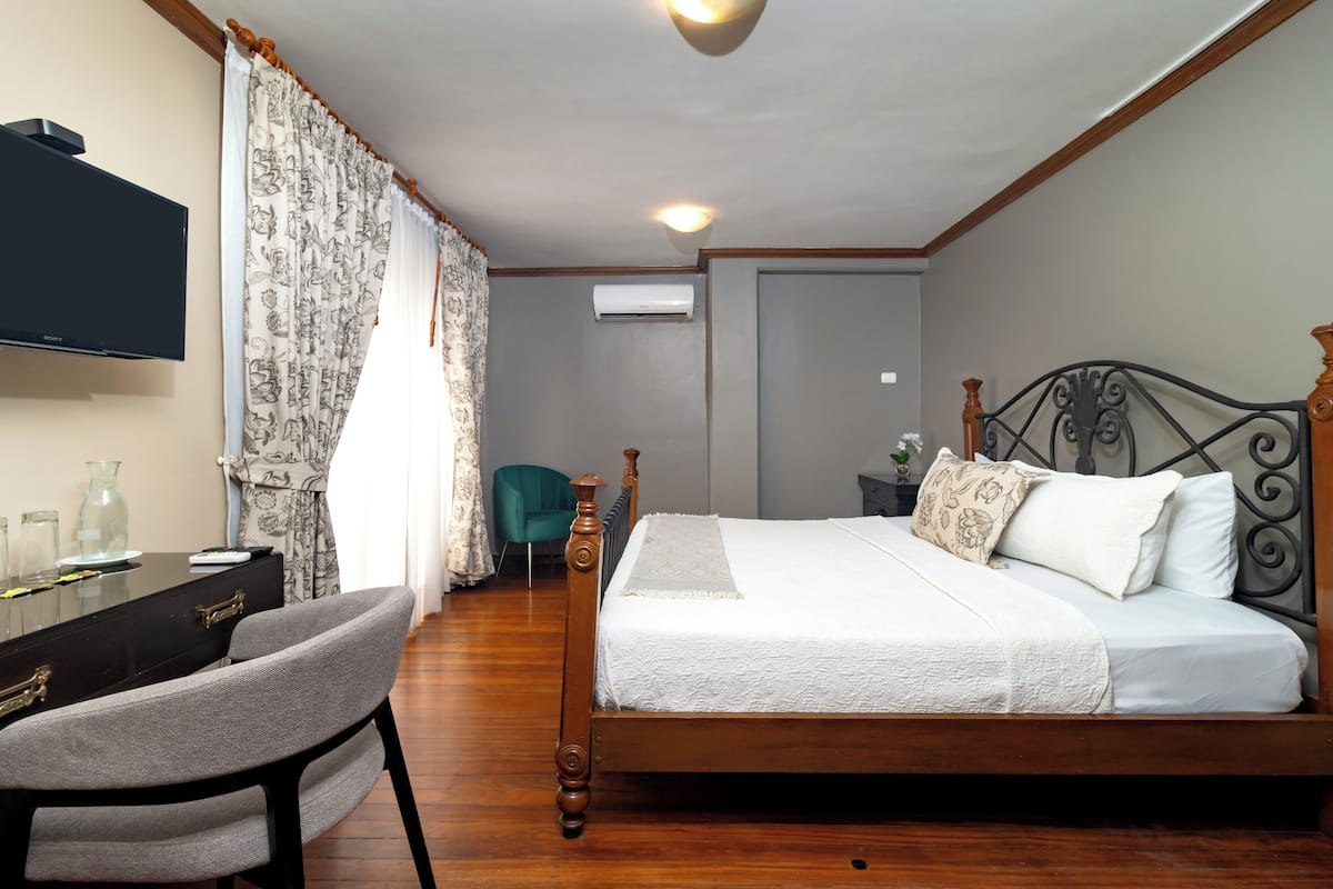 Une chambre à coucher avec un lit en bois, un bureau avec une chaise, une télévision et un fauteuil de couleur turquoise.