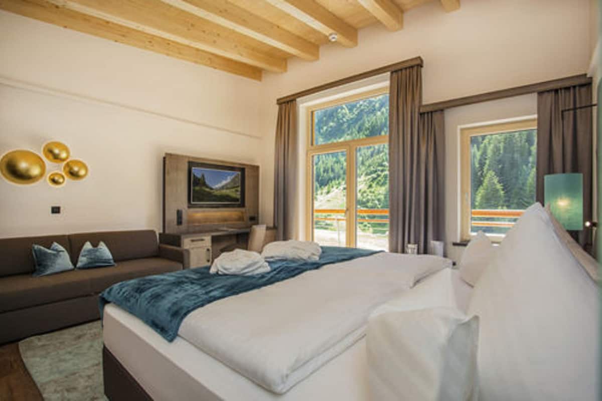 A bedroom with a bed, a sofa, a TV, and a window with a view of trees.