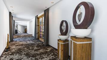 Um corredor com carpete estampado, colunas de madeira com detalhes brancos e uma grande decoração circular na parede.