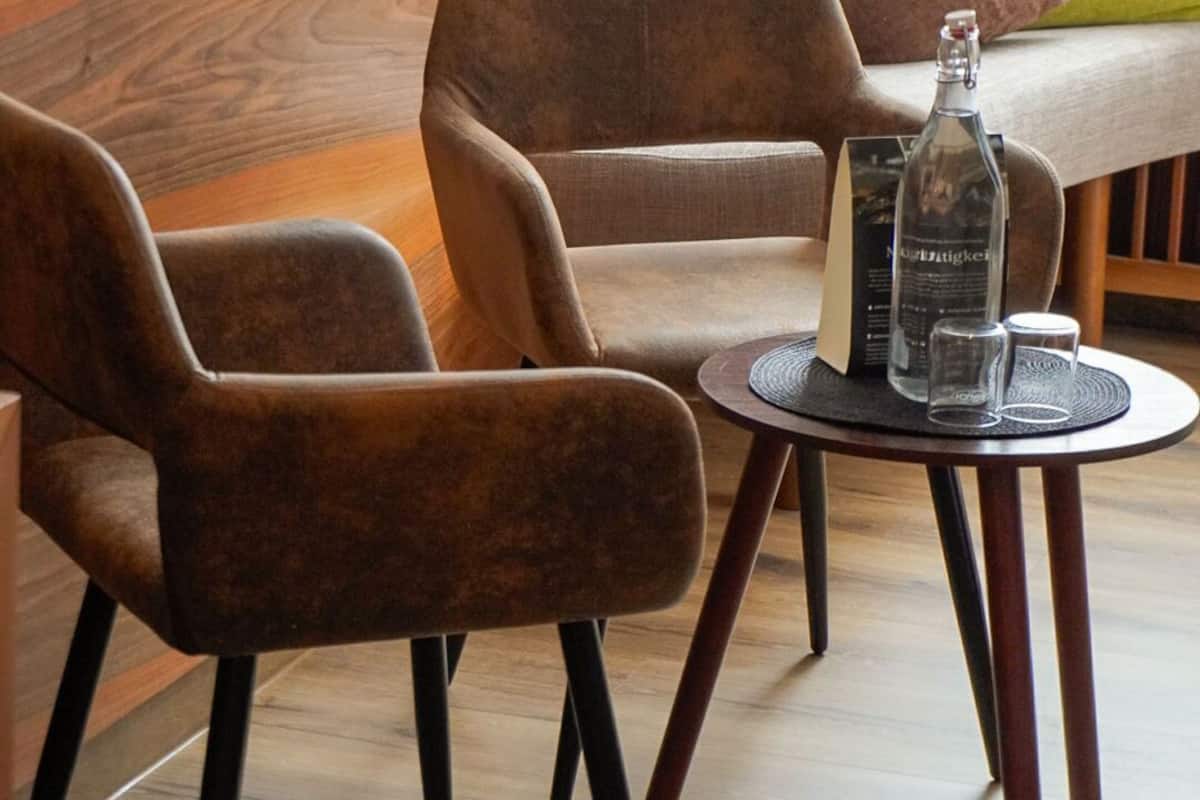 A modern lounge area with a sofa, two armchairs, and a small round table with a bottle and glasses.