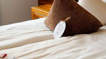 Un lit bien fait, avec du linge de lit blanc et un oreiller marron orné d’une étiquette.