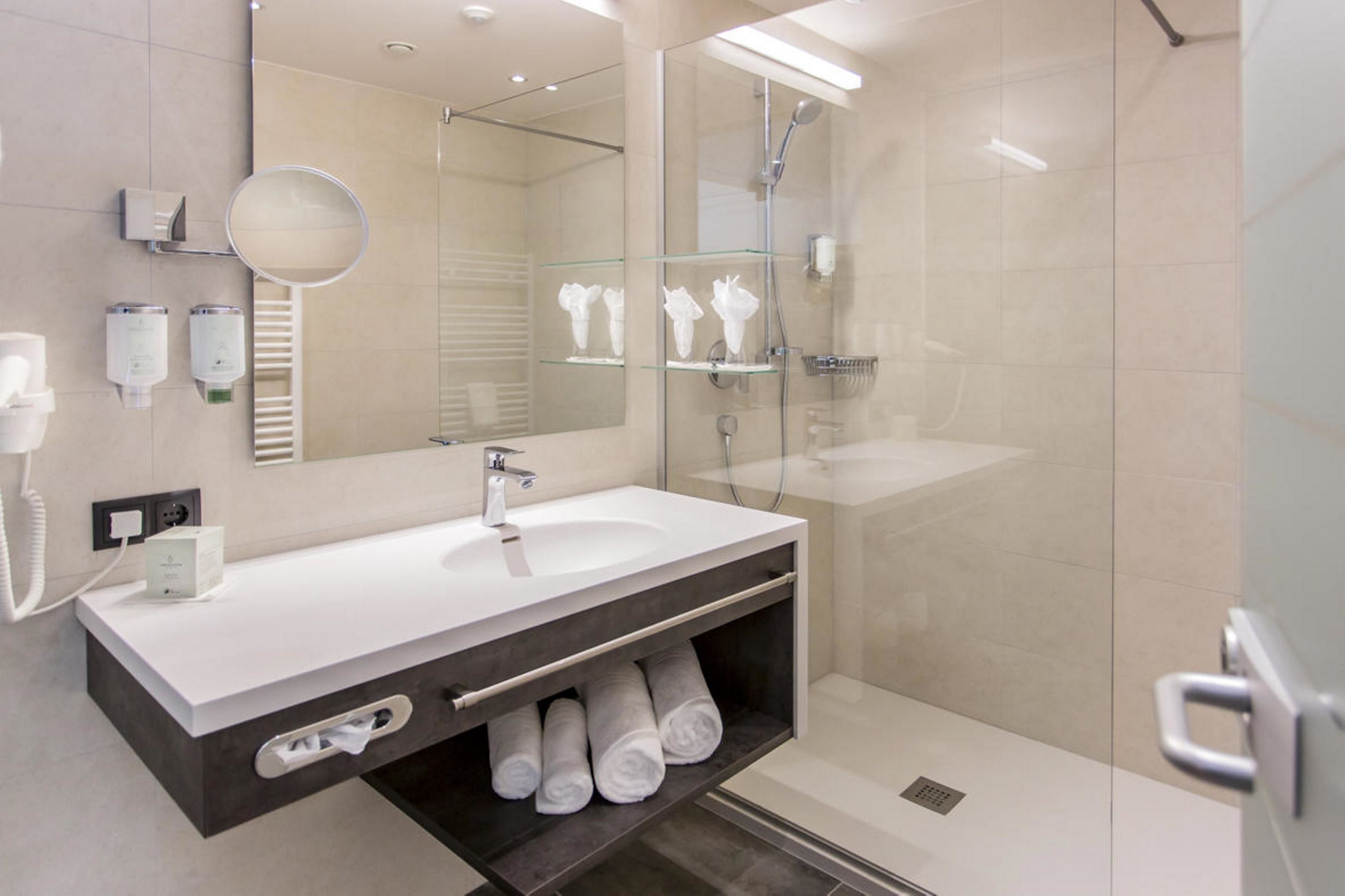 Un baño moderno con un espejo grande, un lavabo blanco y una cabina de ducha de vidrio.