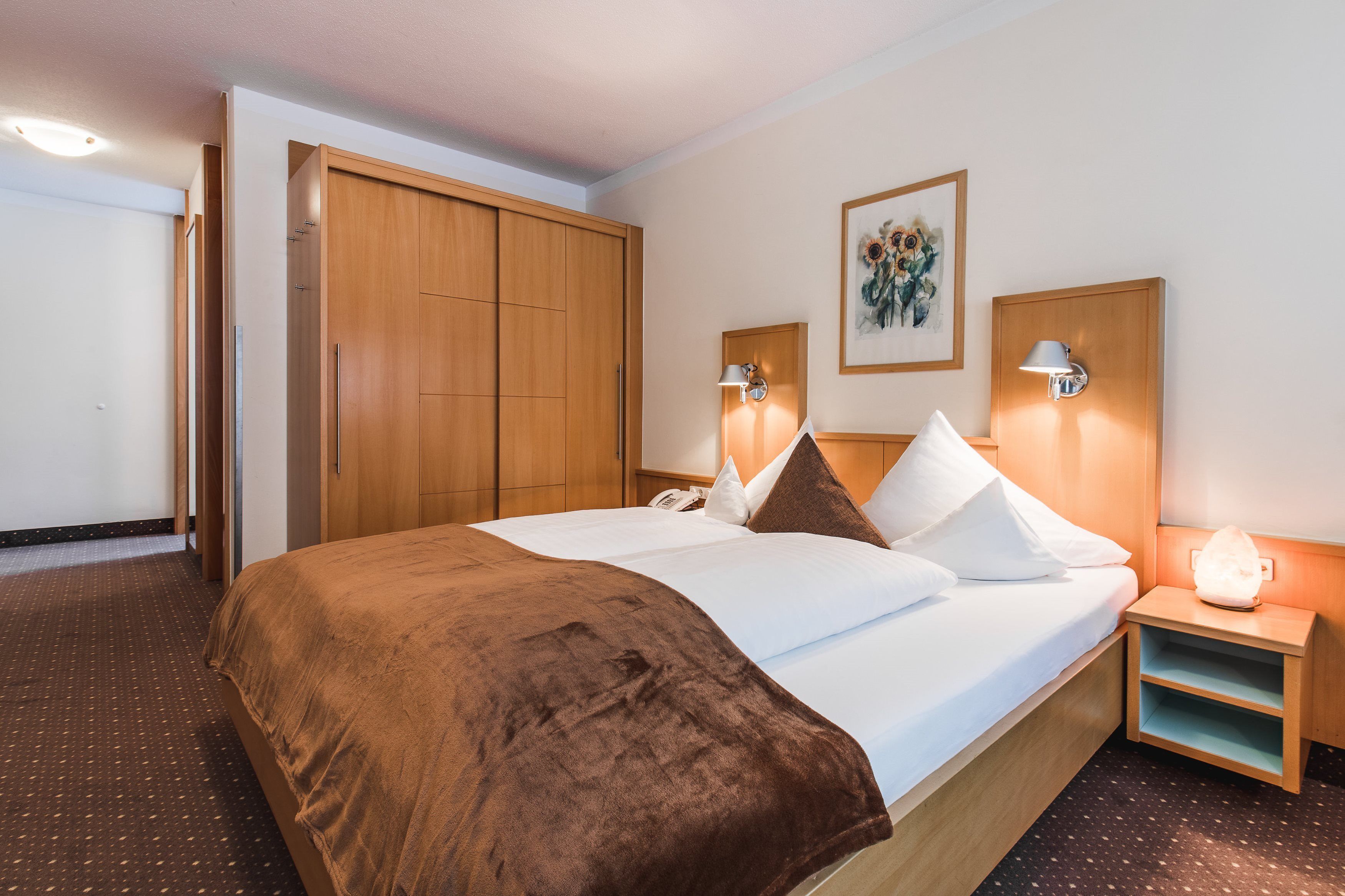 Habitación de hotel con una cama grande, armario de madera, lámparas de noche y una obra de arte enmarcada en la pared.