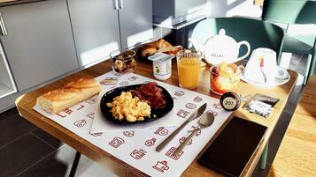 Een ontbijttafel met croissants, roerei, spek, een vruchtensap en een koffiepot.