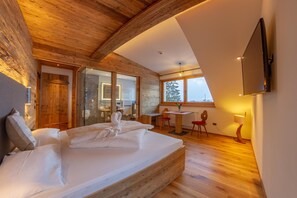 A bedroom with a wooden ceiling, a bed, a desk, and a TV mounted on the wall. - Rosengarten (Dobbiaco)