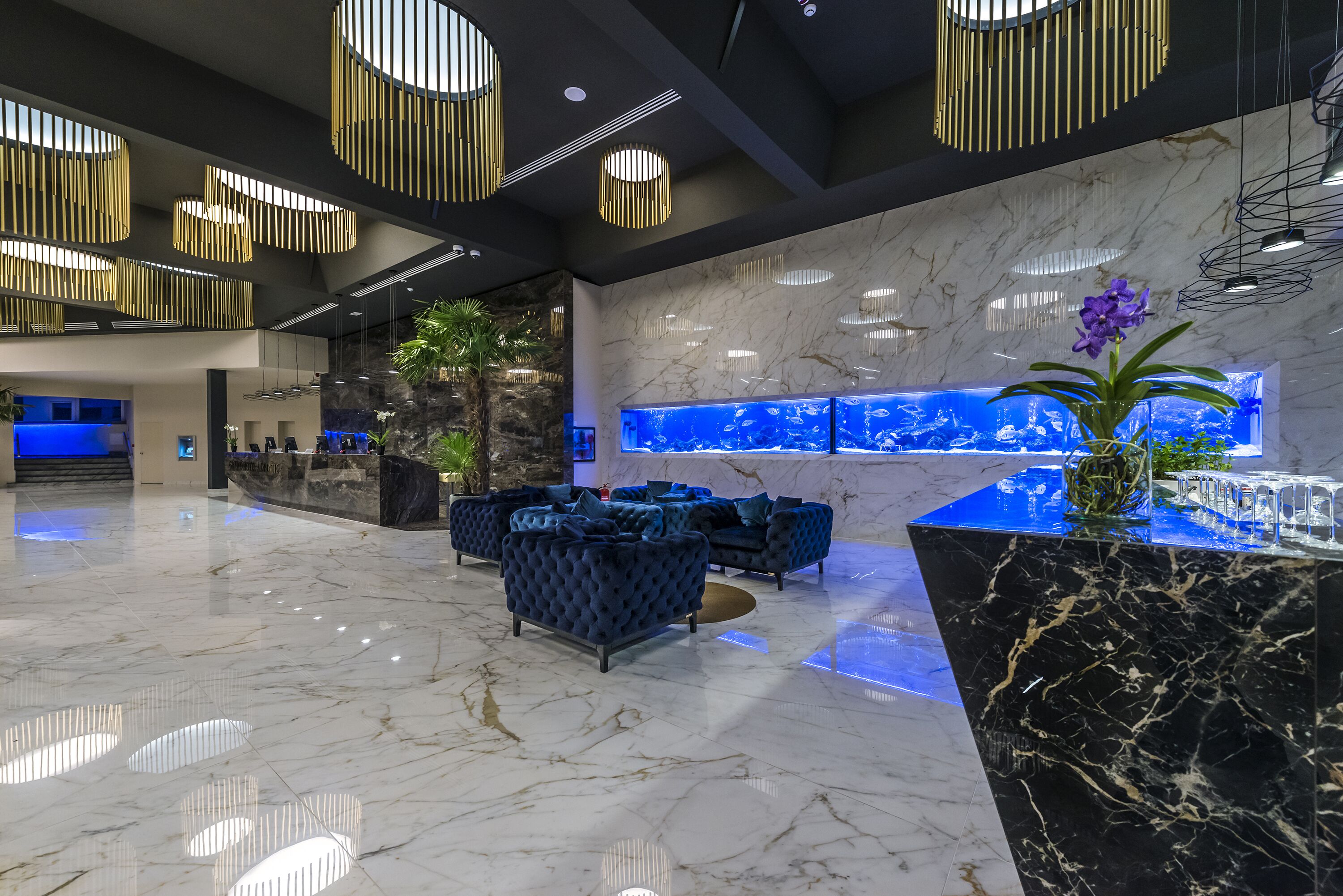 A modern lobby with marble flooring, blue sofas, a reception desk, and a large aquarium.