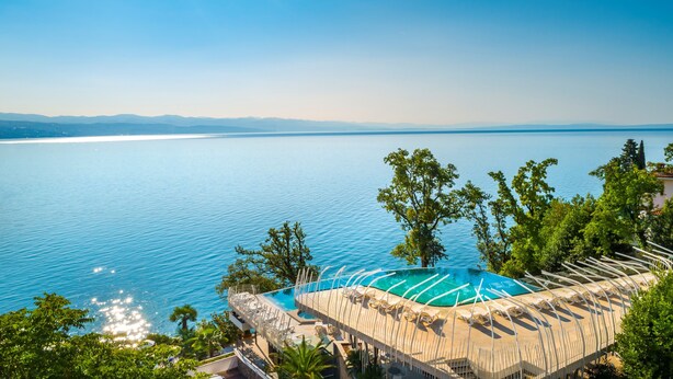 A pool with a view of the sea, surrounded by trees and a building with a unique roof design. - Grand Hotel Adriatic II (Opatija)