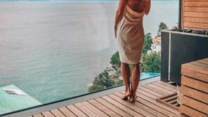 A woman standing on a wooden deck overlooking a body of water with a view of distant land and trees. - Grand Hotel Adriatic II (Opatija)
