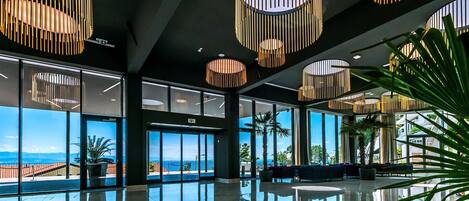A spacious lobby with large windows, a reflective marble floor, and modern circular light fixtures.