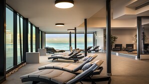 A sunlit room with large windows overlooking a body of water, featuring lounge chairs and a small seating area. - Grand Hotel Adriatic II (Opatija)