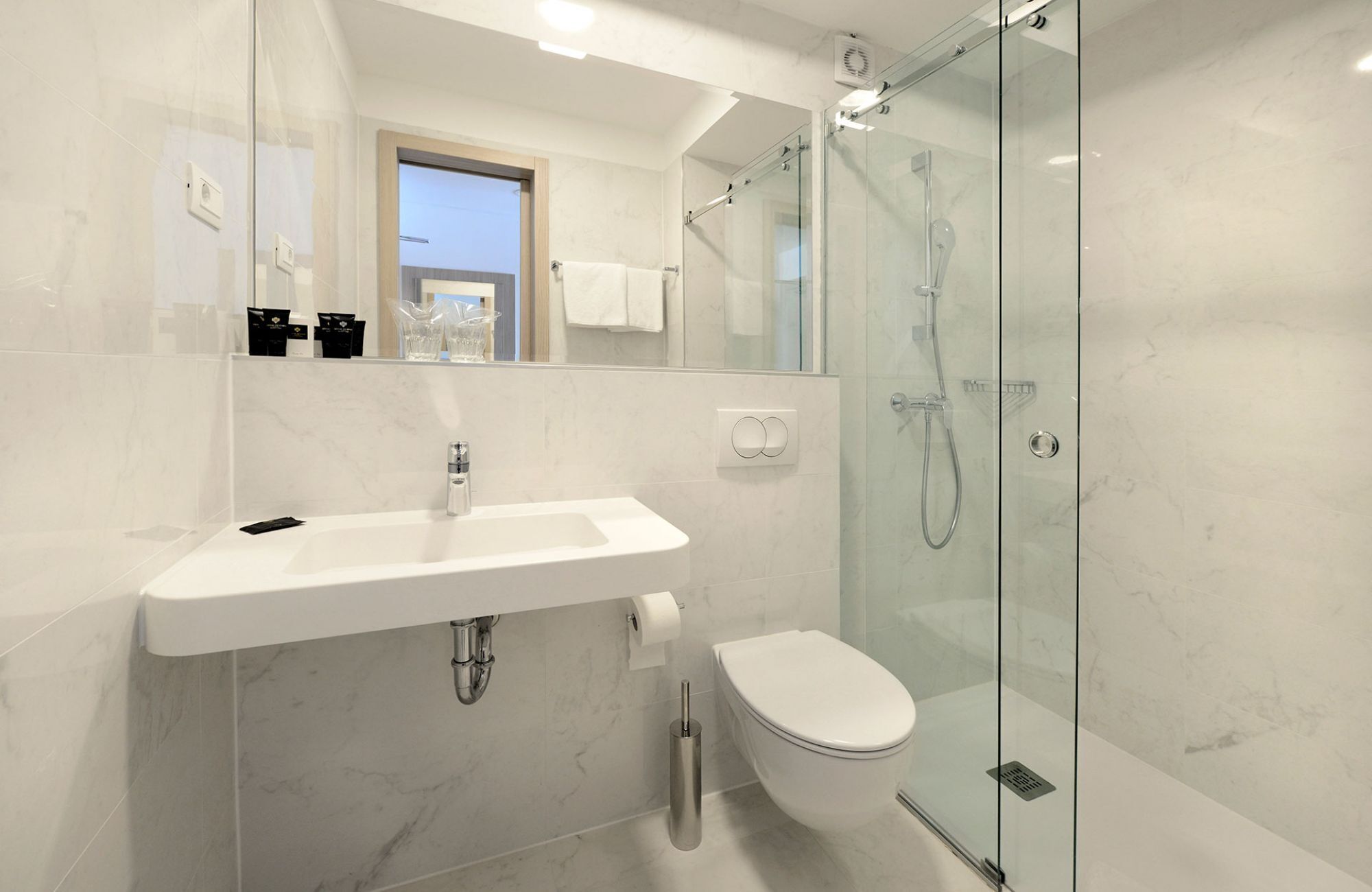 Een moderne badkamer met een douchecabine van glas, een witte wastafel en een toilet.