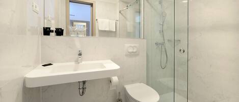 Een moderne badkamer met een douchecabine van glas, een witte wastafel en een toilet.