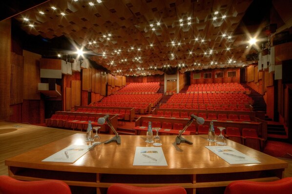 Un teatro con escenario de madera, asientos rojos y un techo con luces que simulan estrellas.
