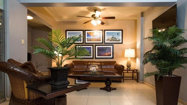 A living room with a brown leather sofa, a coffee table, a floor lamp, and two potted plants. - Hotel Mazatlan (Mazatlán)