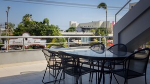 A rooftop terrace with a round glass table and black metal chairs, overlooking a cityscape with buildings and palm trees. - Hotel Mazatlan (Mazatlán)