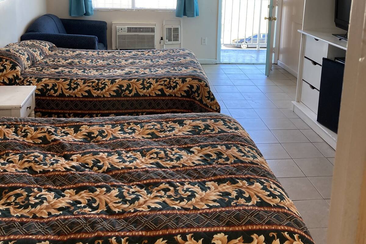 A hotel room with two beds, a TV, a balcony, and a ceiling fan.