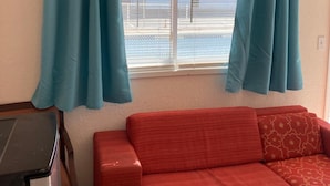 Una habitación con un sofá rojo, una ventana con cortinas azules y vistas a un edificio.