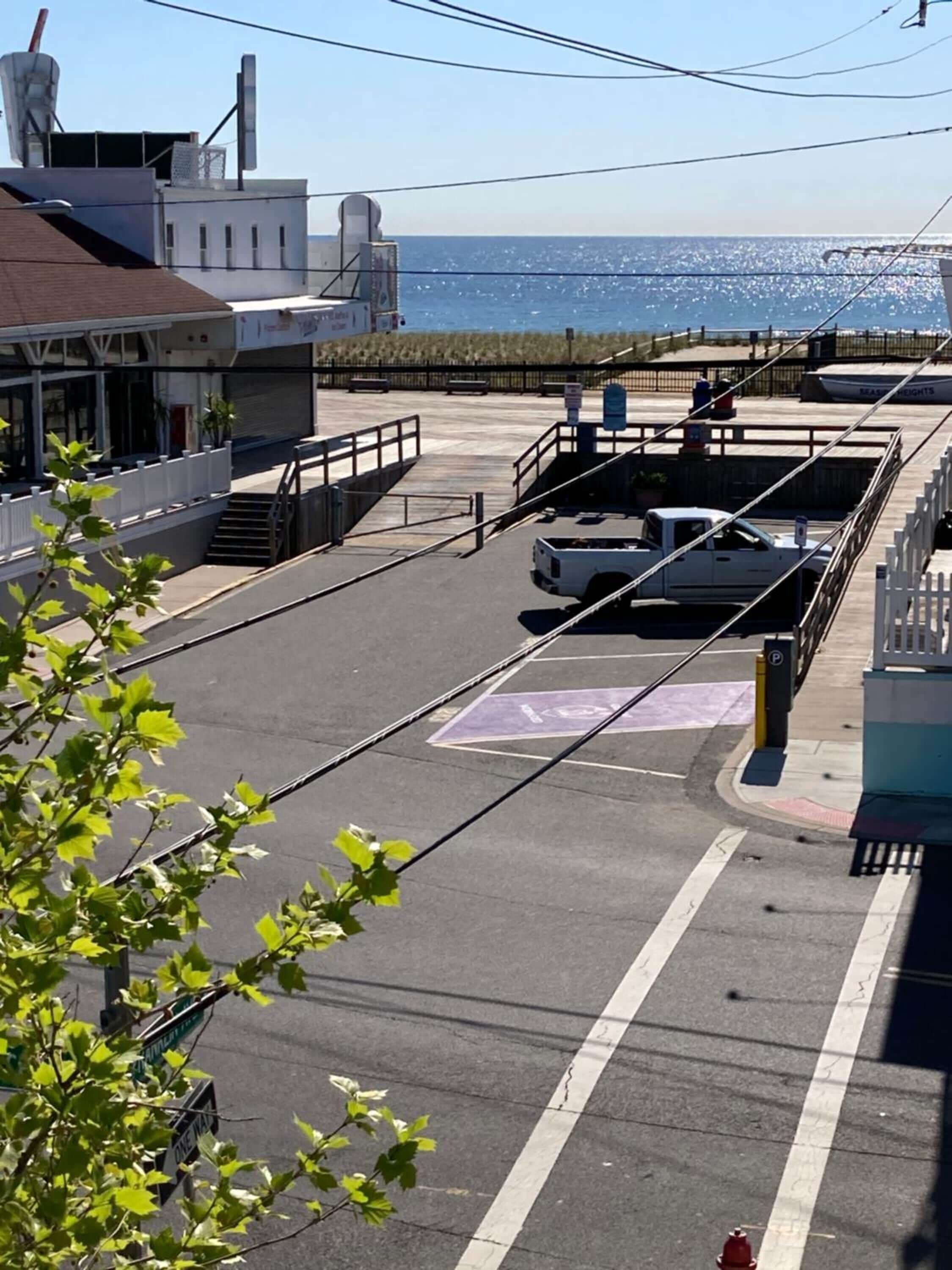 A parking lot with a white truck, a pedestrian crossing, and a view of the ocean.