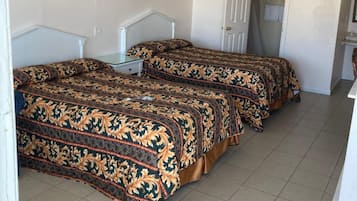 Een kamer met twee bedden, elk voorzien van een bedovertrek met patroon, een witte hoofdbord en een klein tafeltje. Er hangen afbeeldingen in lijsten aan de muur en is een deur naar een andere kamer.