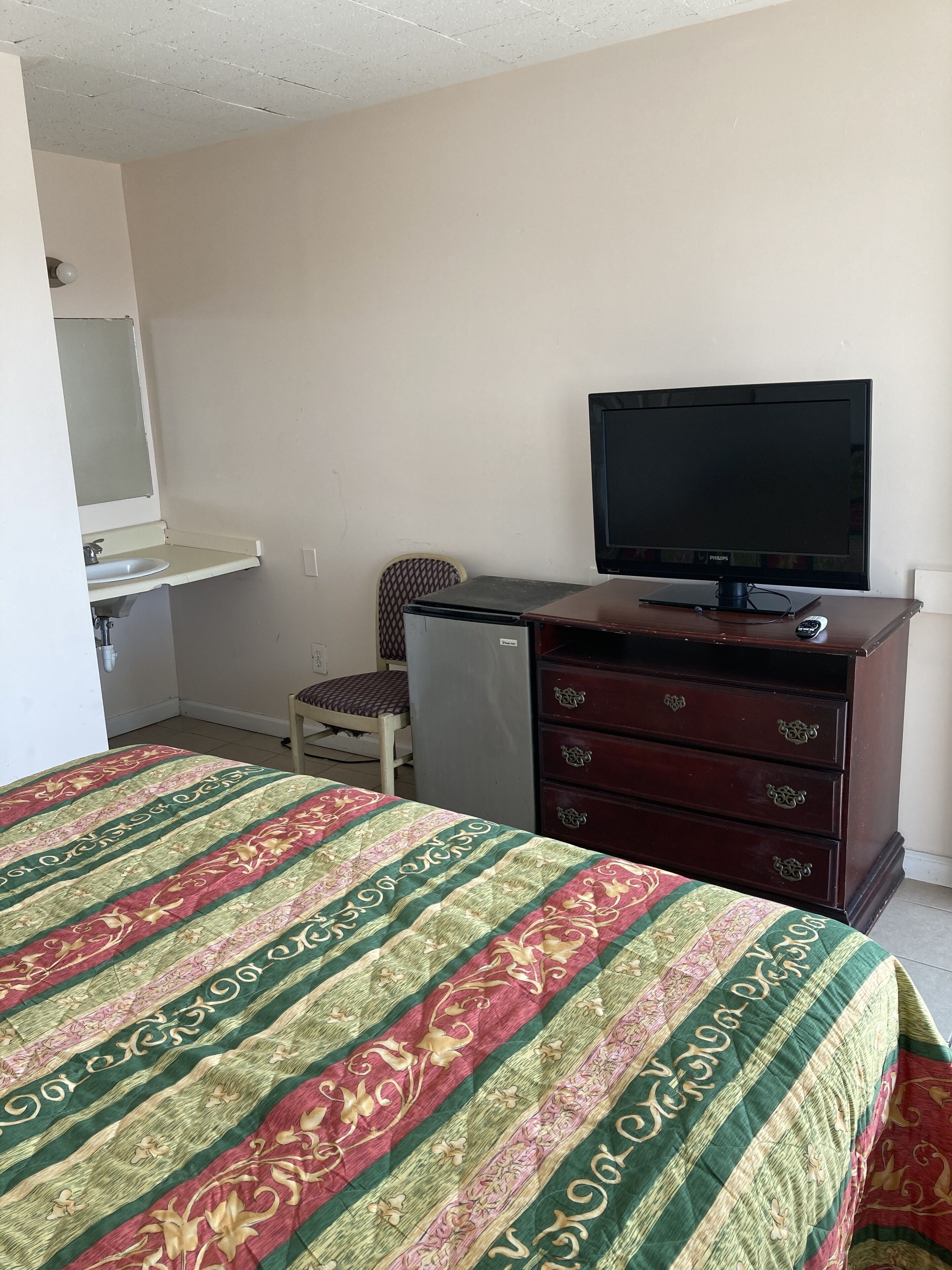 Une chambre d’hôtel équipée d’un lit, d’une télévision, d’un petit réfrigérateur, d’une commode et d’une chaise.