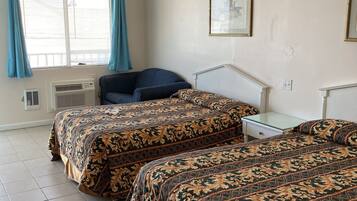 A room with two beds, a chair, a small table, and a window with curtains.