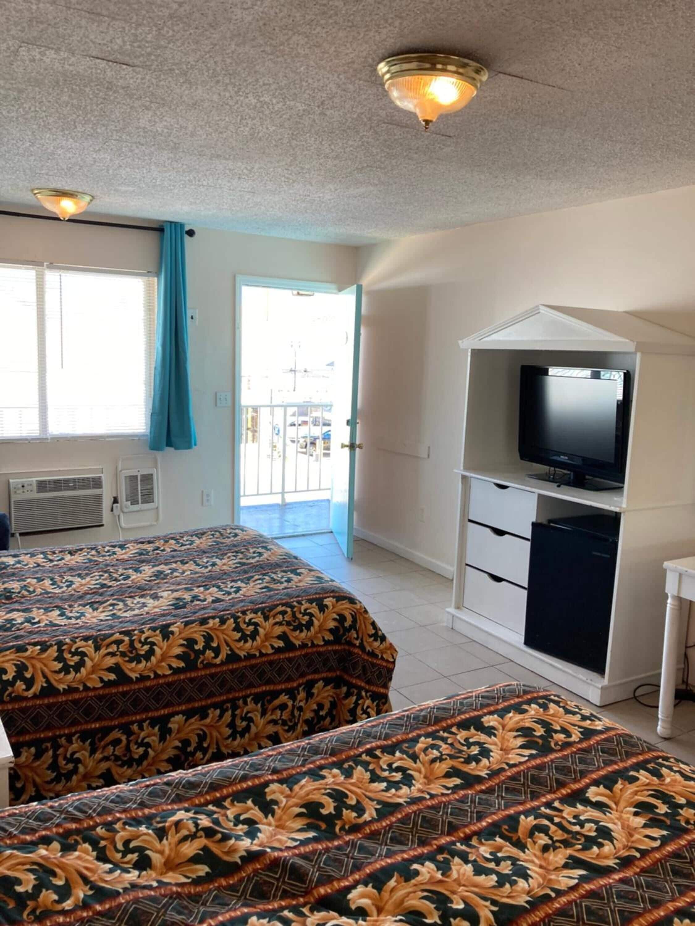 A hotel room with two beds, a television, a small desk, and a balcony with a view.