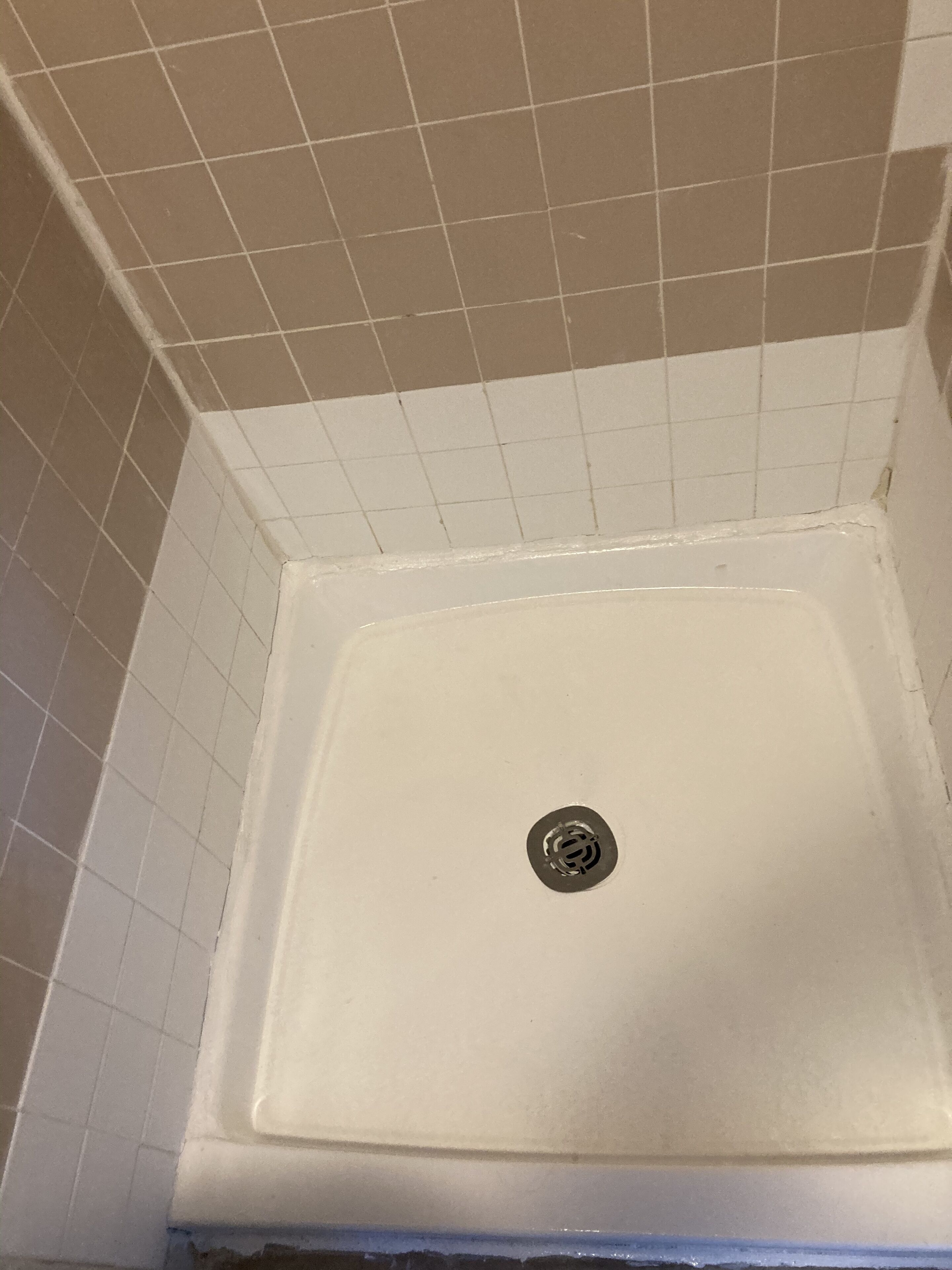 A bathroom with a white tiled floor and walls, a white bathtub, and a visible drain in the center.