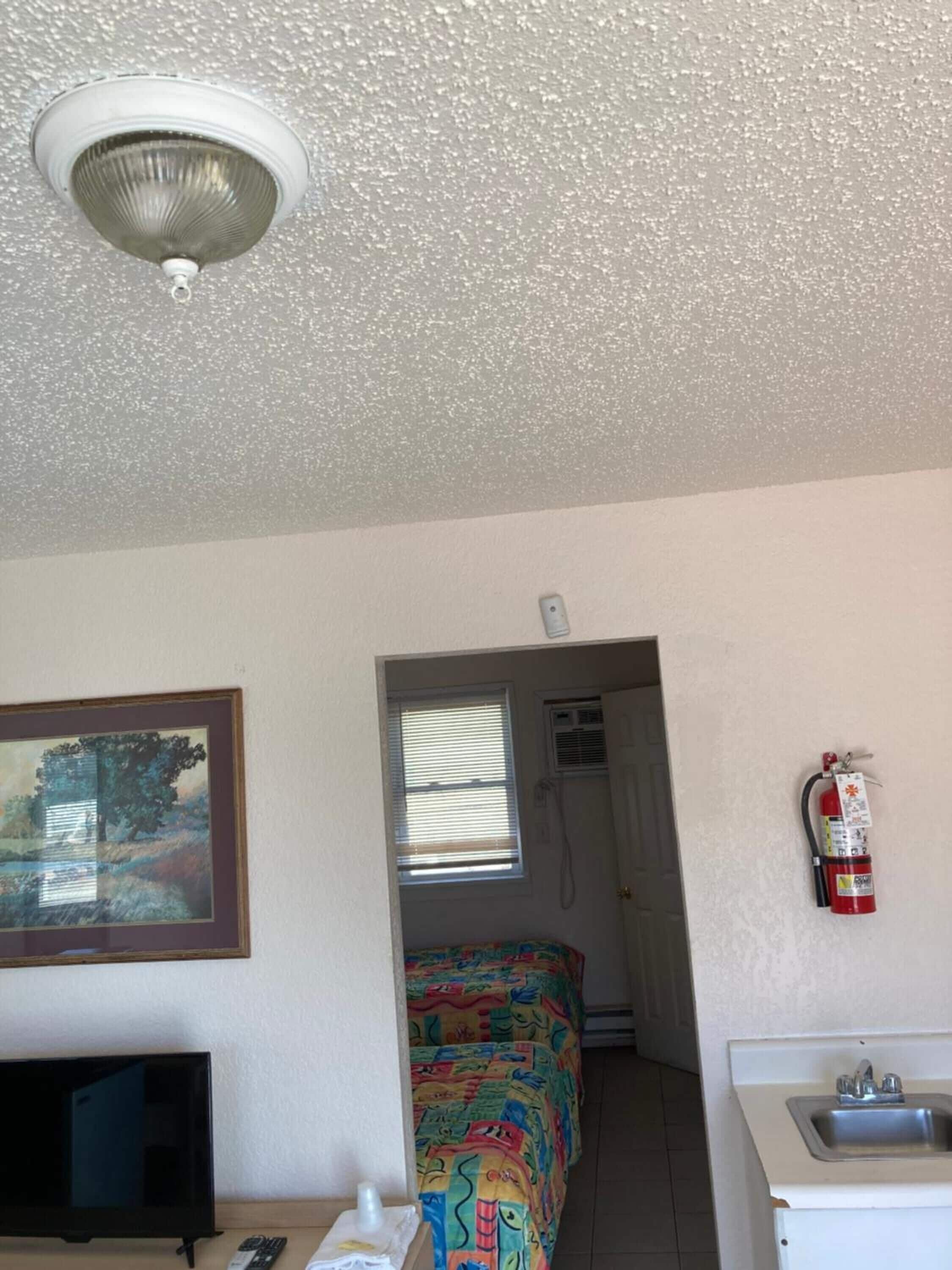 A small, compact room with a bed, a television, a sink, and a fire extinguisher.
