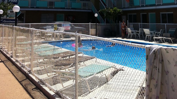 Un hotel con zona de piscina, varios balcones y un cartel que indica la presencia de socorrista.