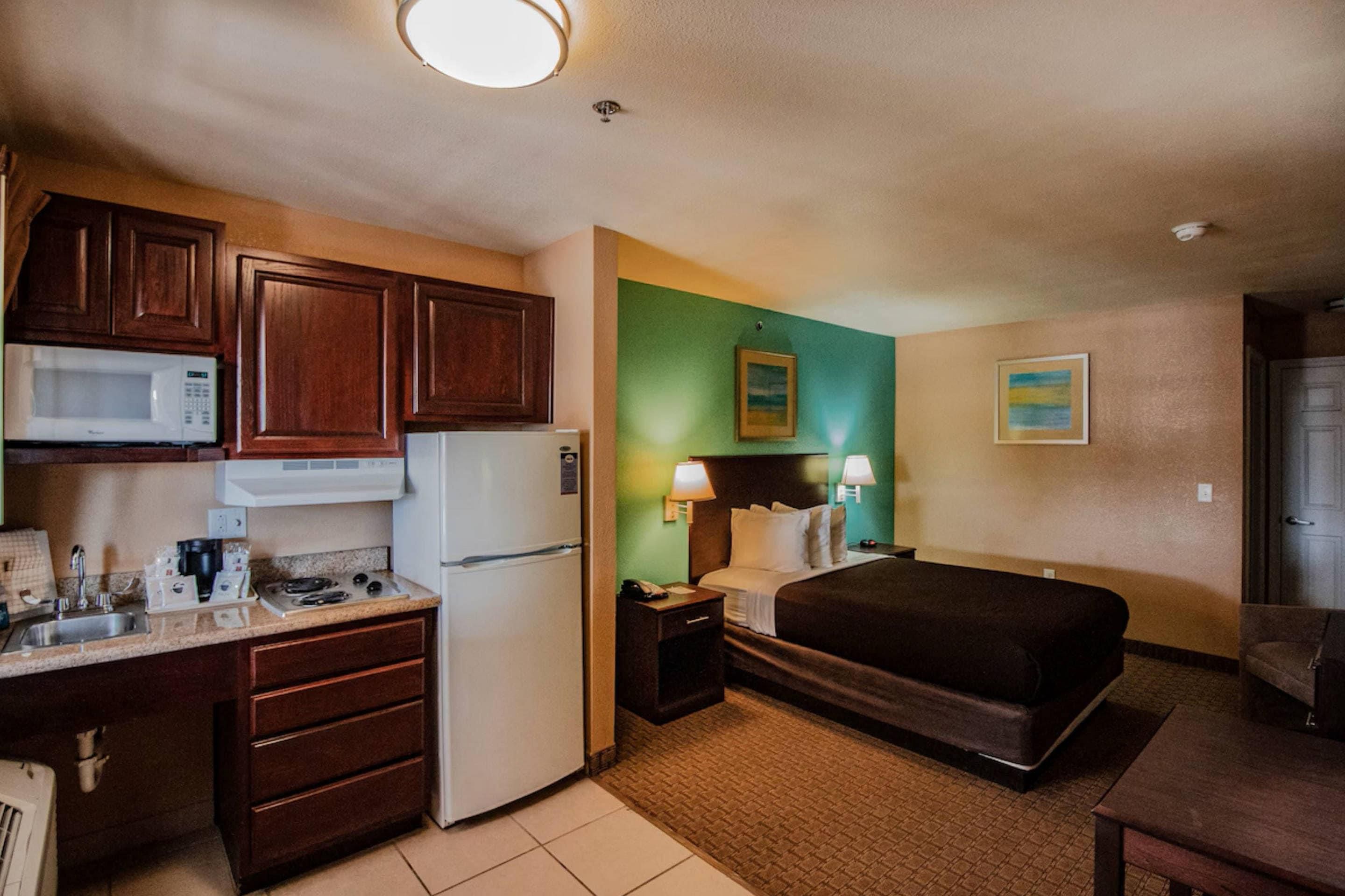 Een compacte hotelkamer met een kitchenette, een bed, een bureau en een klein zithoekje.
