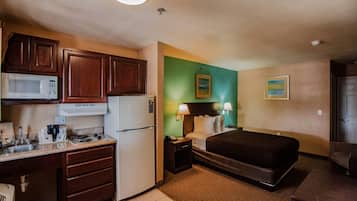Een compacte hotelkamer met een kitchenette, een bed, een bureau en een klein zithoekje.