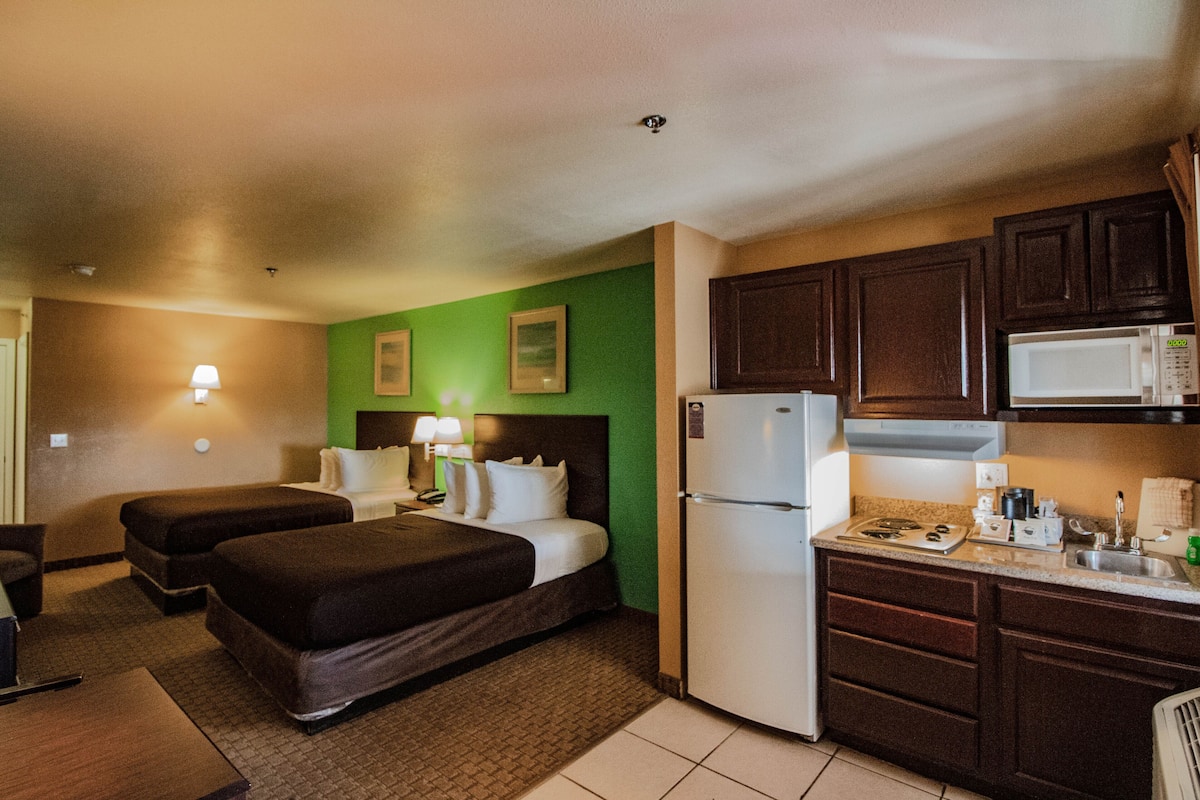 A hotel room with two beds, a kitchenette, and a green accent wall.