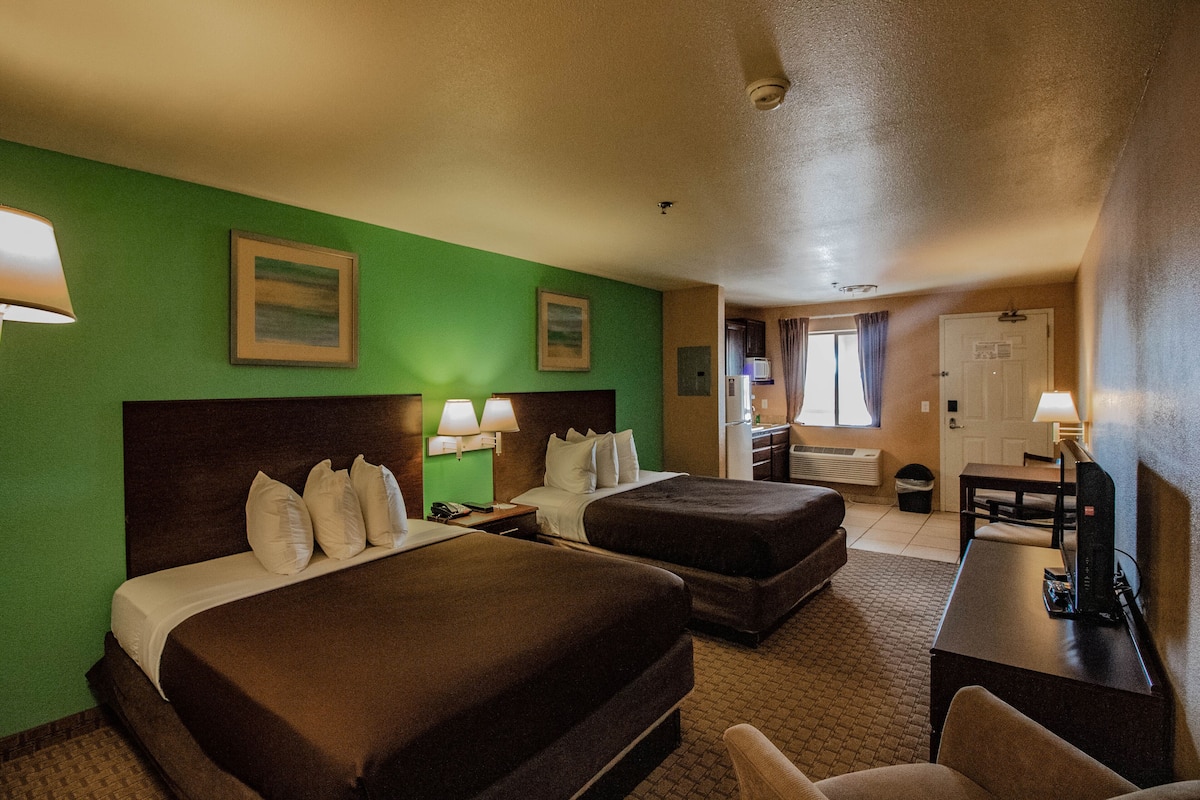 A hotel room with two beds, a desk, a chair, and a TV.