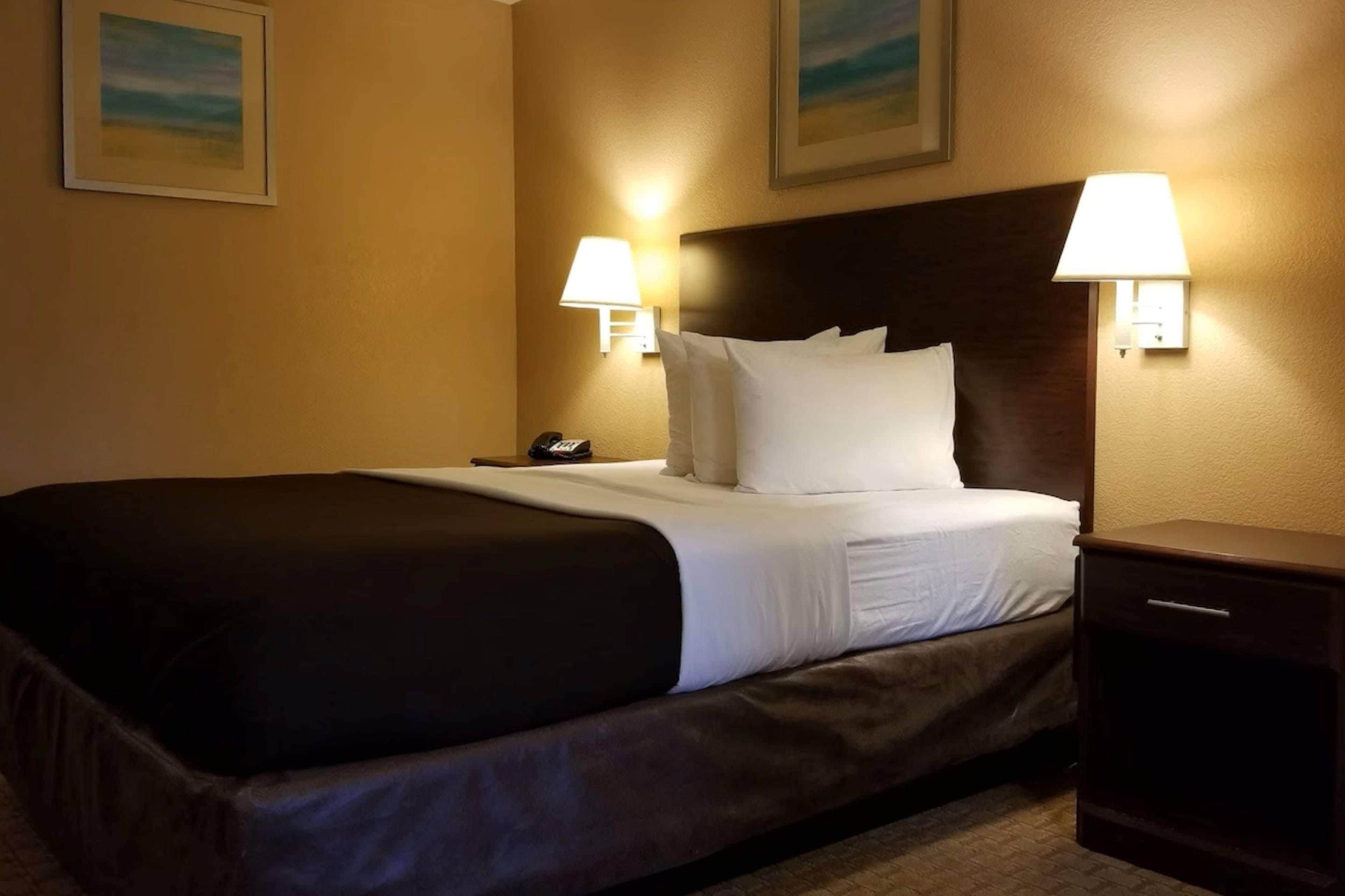 A hotel room with a large bed, two bedside lamps, a nightstand, and two framed pictures on the wall.