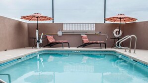 Una piscina interior con dos sillas de descanso y dos sombrillas. Se ve un cartel que prohíbe el clavado.