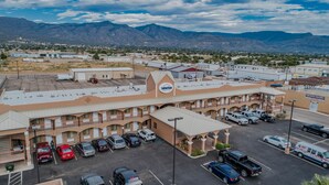 Un motel con un letrero central, varios espacios de estacionamiento y montañas al fondo.