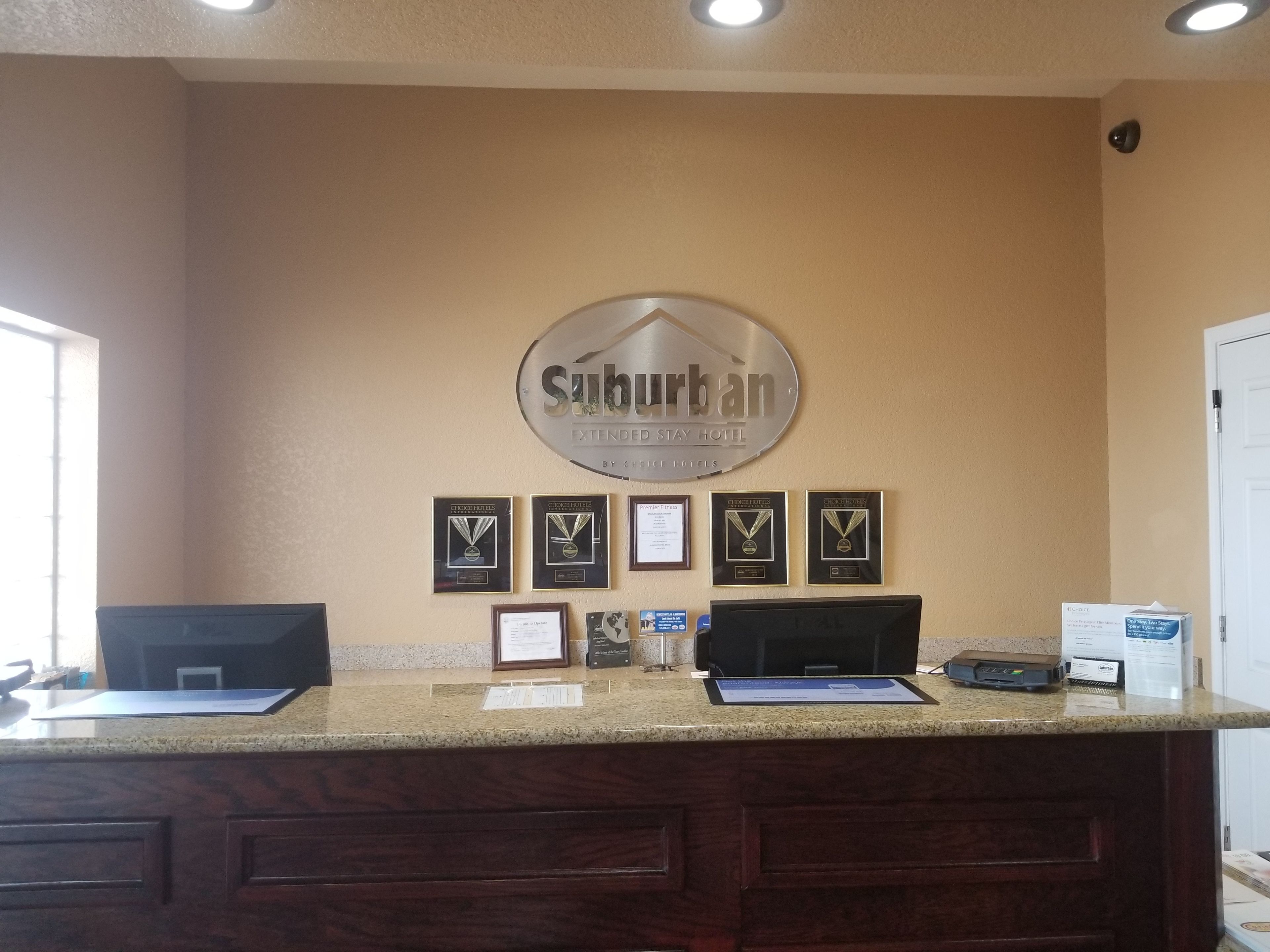A reception desk with a sign reading "Suburban Extended Stay Hotel" and several framed awards on the wall.