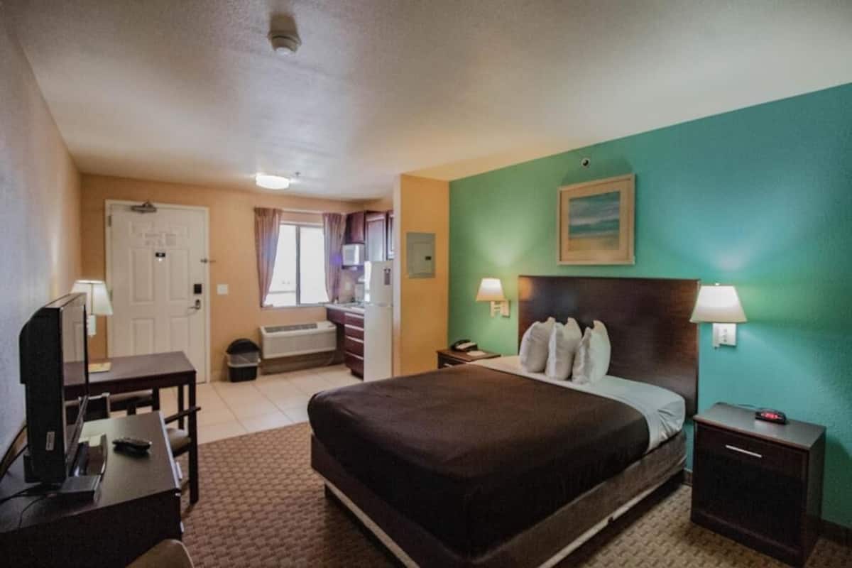 A hotel room with a bed, bedside tables, a desk, a mirror, a television, and a window.