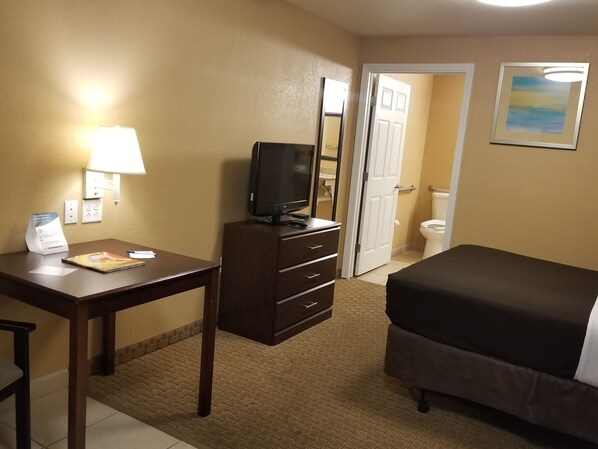 Una habitación de hotel con escritorio, televisor, cama, baño y un cuadro en la pared.