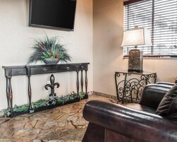 Un vestíbulo con suelo de piedra, una consola de madera oscura con una planta, un sofá de cuero negro y un televisor fijado a la pared.