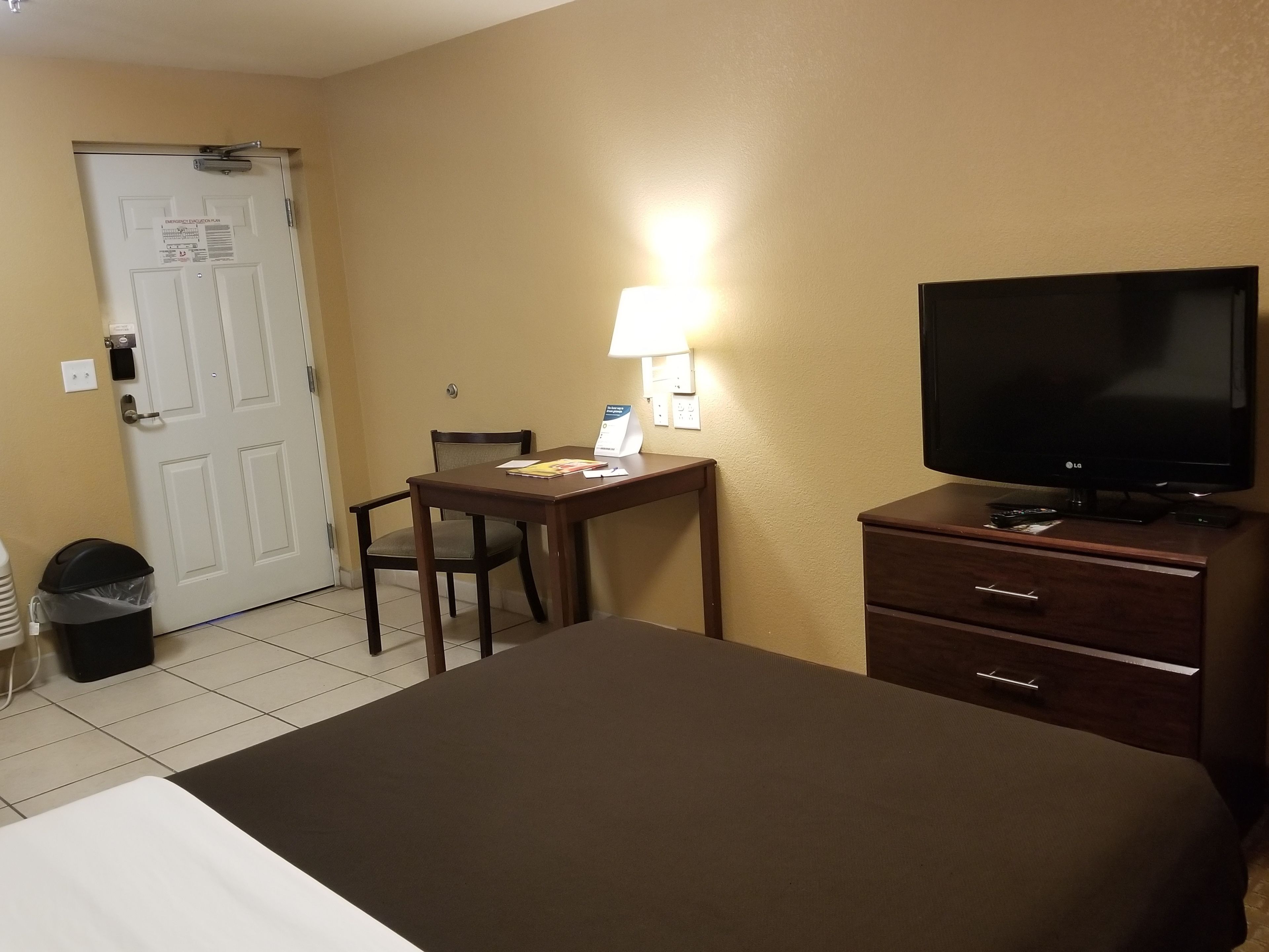 Ein Hotelzimmer mit einem Bett, einem Schreibtisch mit Stuhl, einem Fernseher und einer Lampe.