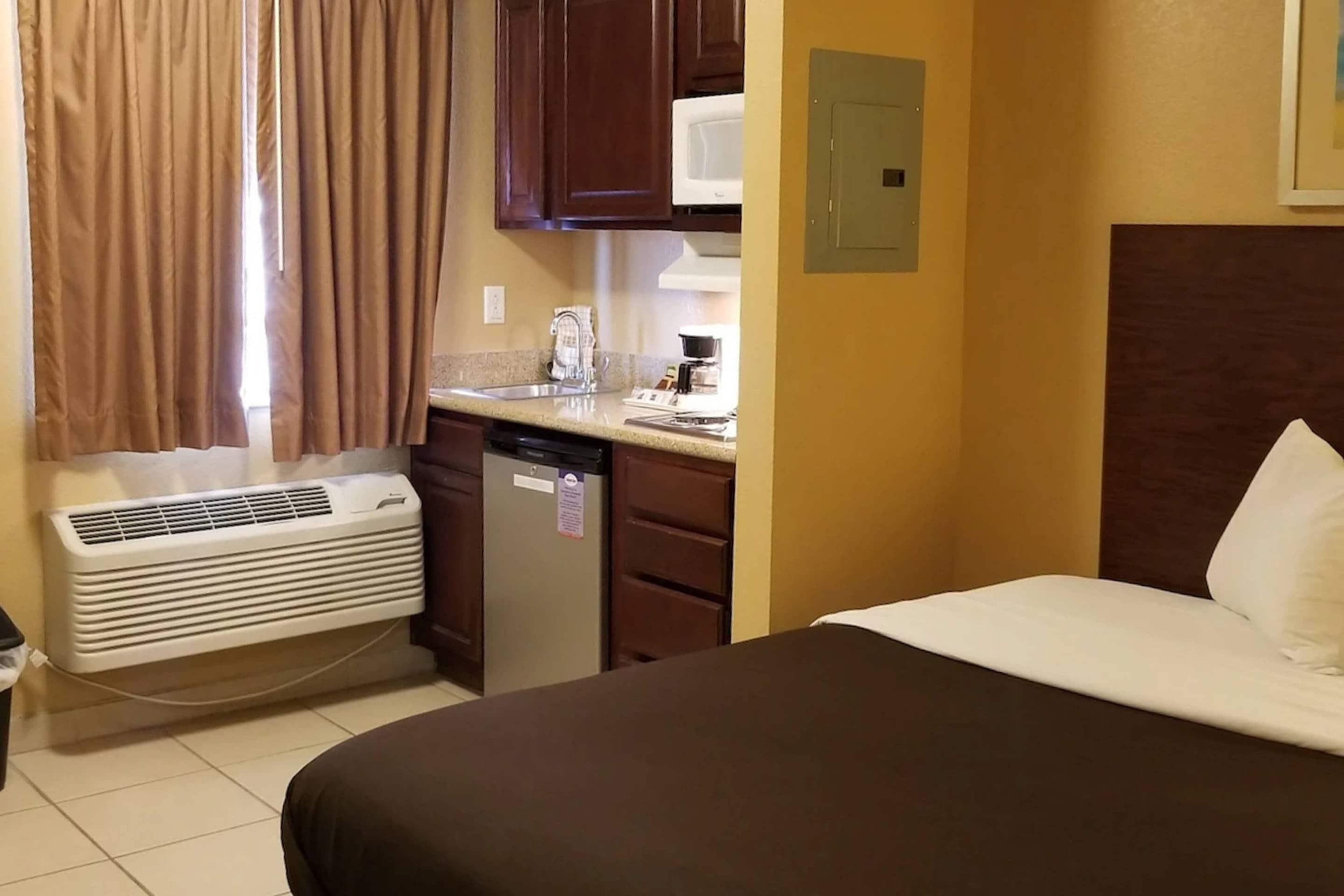 A hotel room with a bed, a kitchenette, a microwave, and a heater.