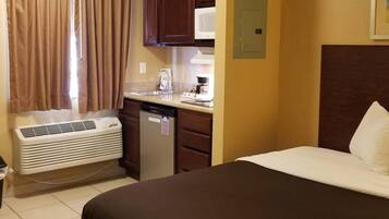 A hotel room with a bed, a kitchenette, a microwave, and a heater.