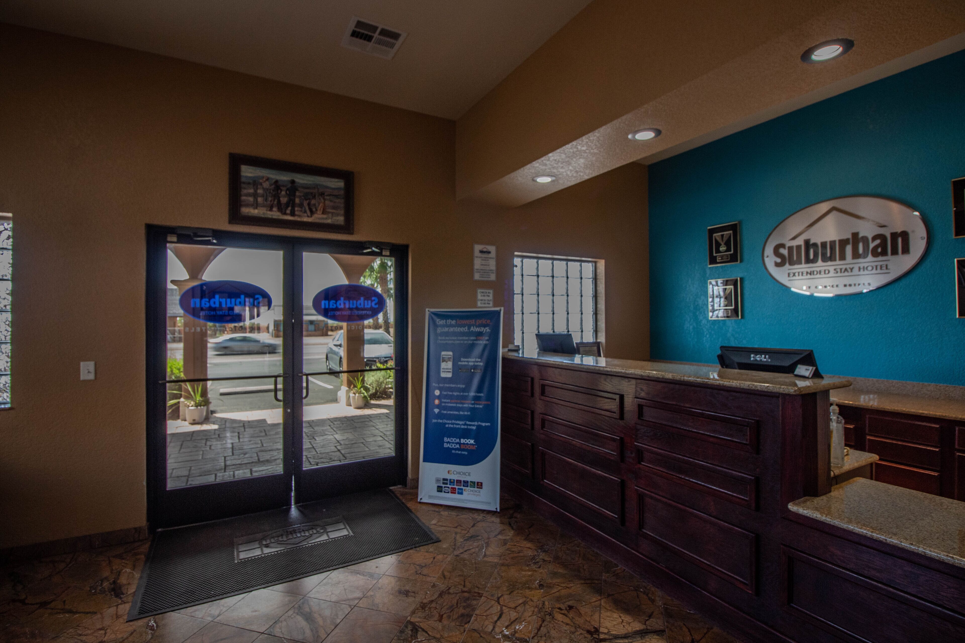 A hotel reception area with a blue wall, a Suburban Extended Stay Hotel sign, a reception desk, and a glass door entrance.