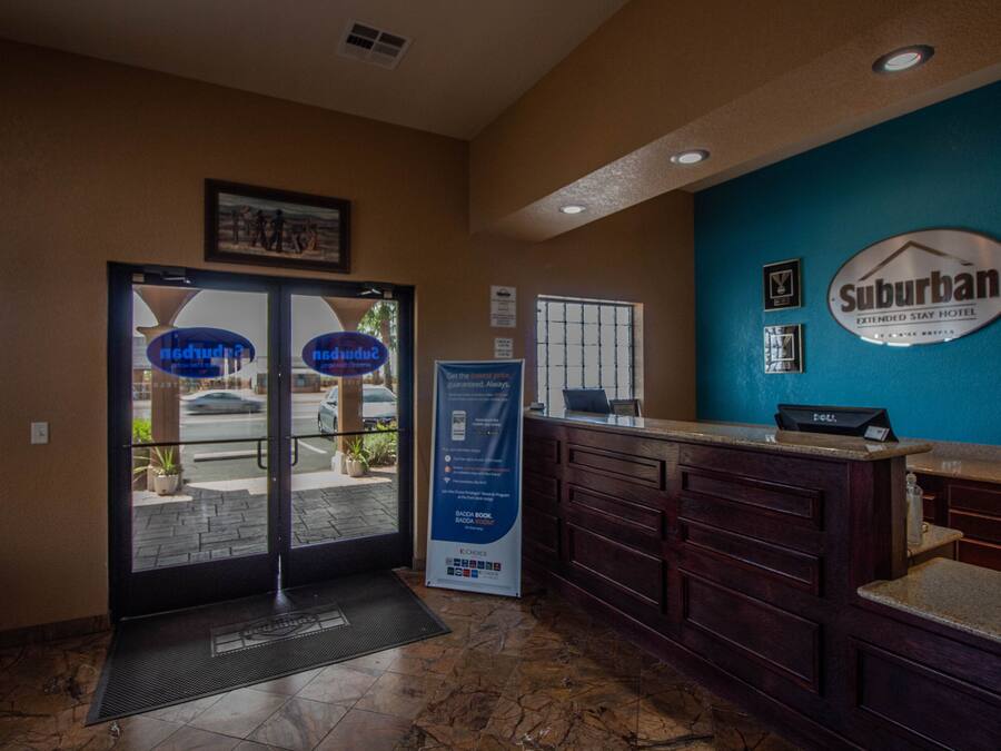 A hotel reception area with a blue wall, a Suburban Extended Stay Hotel sign, a reception desk, and a glass door entrance.