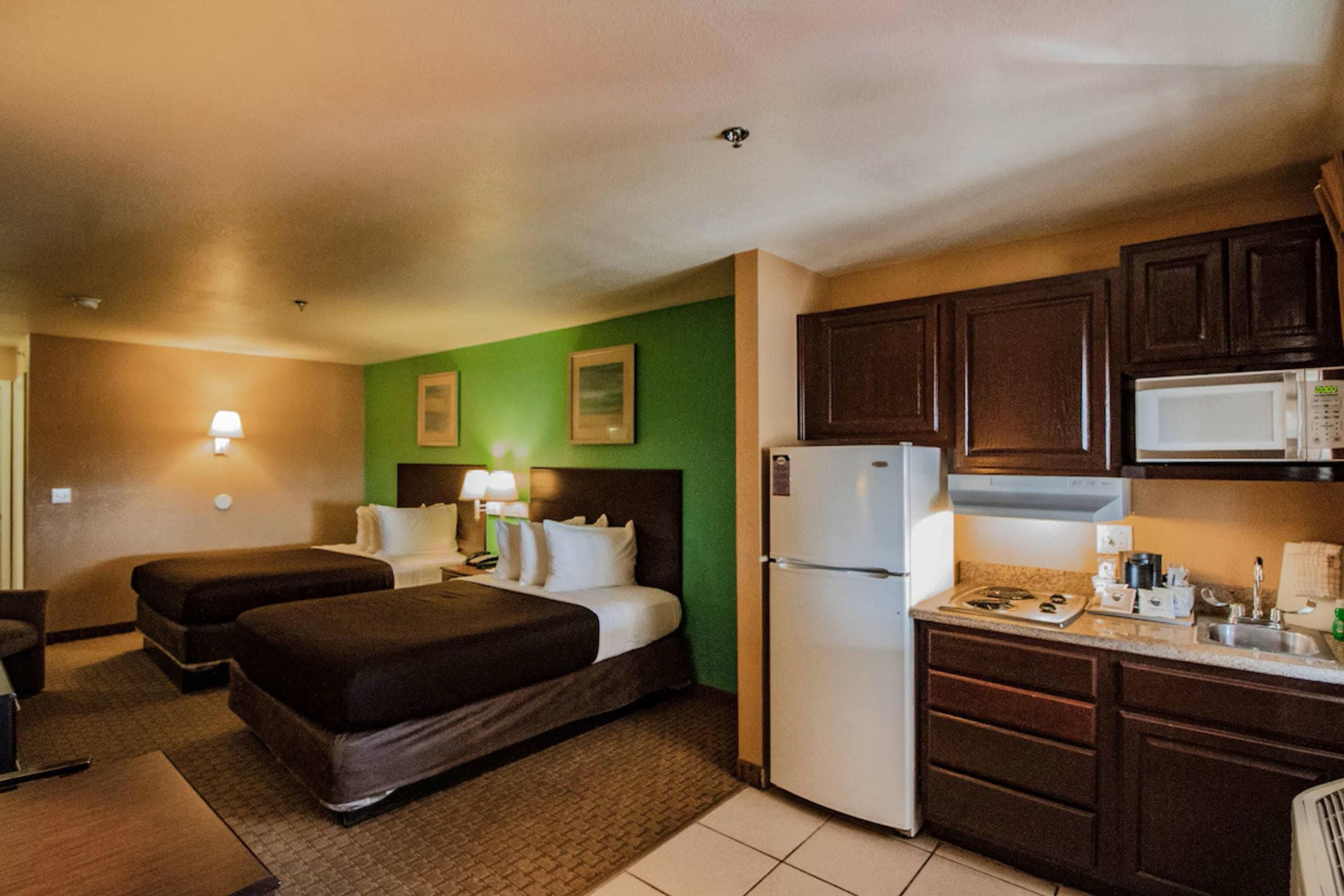 A hotel room with two beds, a kitchenette, and a green accent wall.