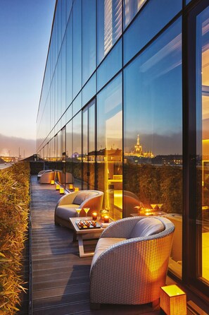 A modern outdoor seating area with wicker chairs and a table, overlooking a cityscape at dusk. - Armani Hotel Milano (Milan)