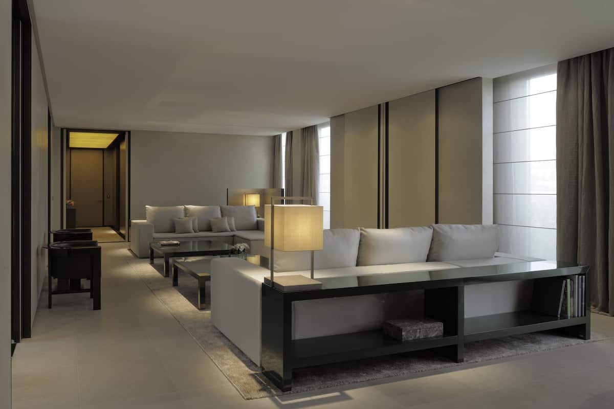 A modern living room with a sofa, coffee table, and lamp. There is a door leading to another room.