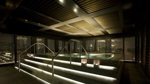 Un área de piscina interior moderna con escalones que bajan al agua, barandales metálicos y un techo con paneles de ventilación.