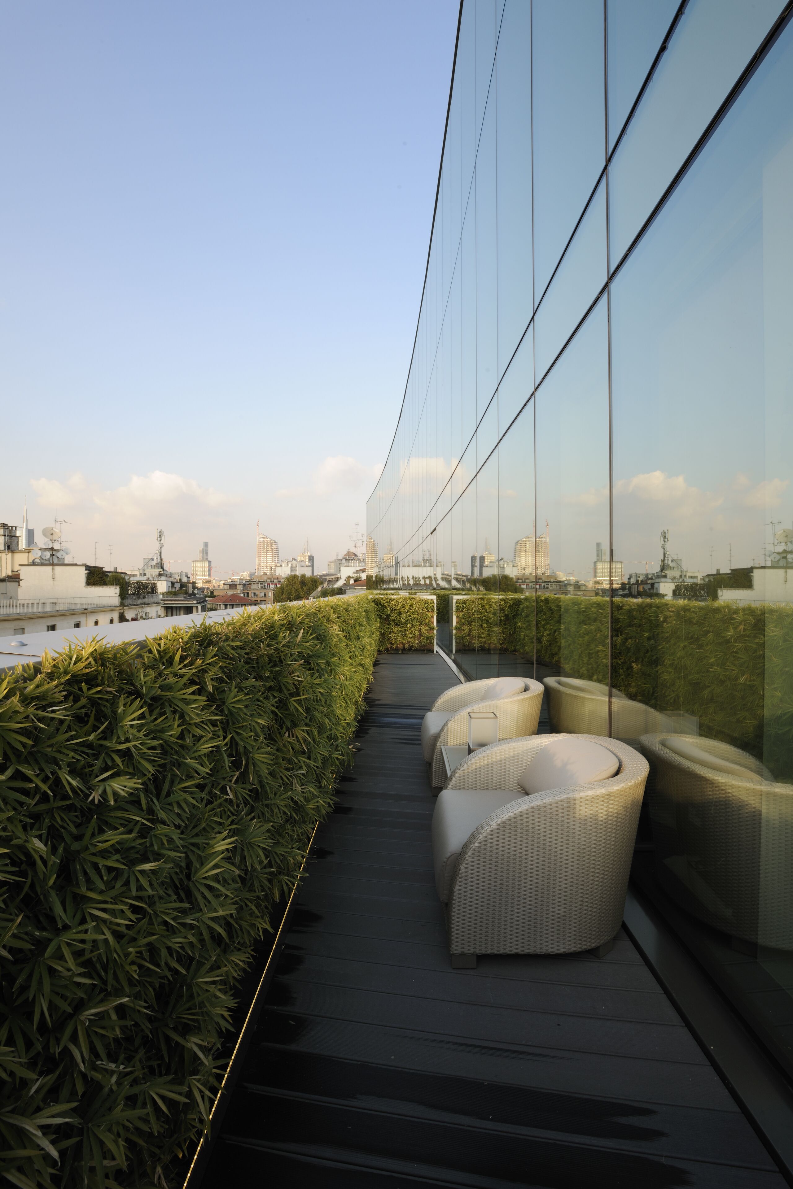 Un'area salotto esterna moderna con mobili in vimini, una parete vetrata e vista sullo skyline della città.